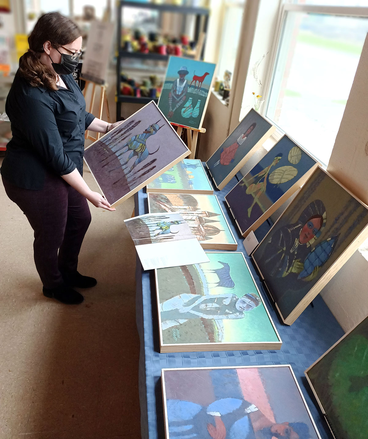 Michelle Cate arranges paintingss donated by Lynn Sweat to The Art Studio's "Raise the Roof" campaign.