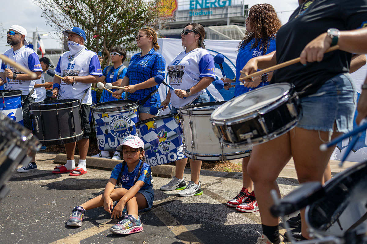 Drummers play cadences as a small girl sits in the parking lot outside of Shell Energy Stadium in Houston, July 4th. UP photo by Brian Quijada.