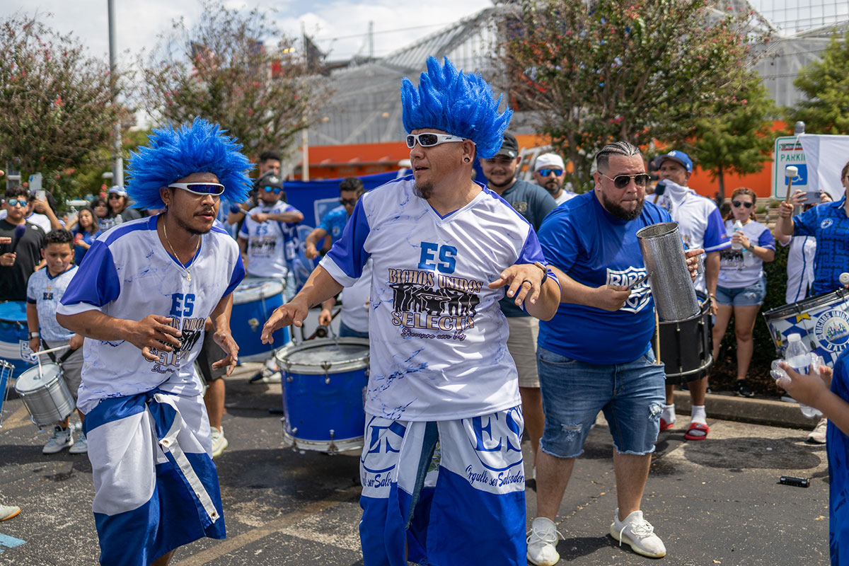 Two ultra members in blue wigs dance as the band plays cadences in the parking lot outside of Shell Energy Stadium in Houston, July 4th. UP photo by Brian Quijada.